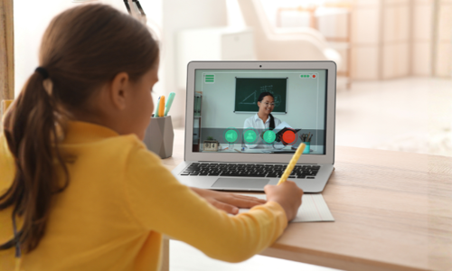 Girl writing in a textbook while watching a math lesson on a laptop