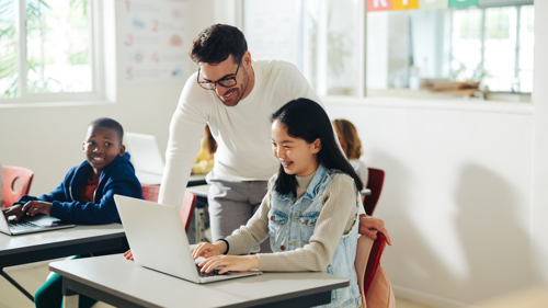 Teacher helps middle school students work on laptops during a classroom lesson