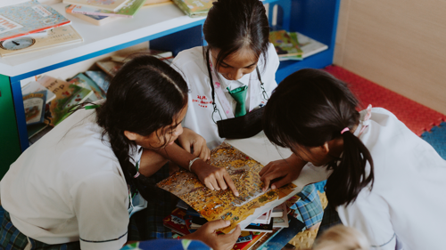 Three students work together on a classroom activity while looking at a colorful puzzle or worksheet
