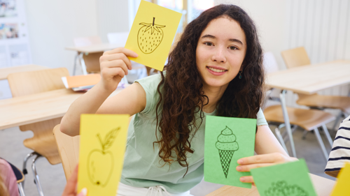 Girl demonstrating hand-drawn flashcards featuring different foods.